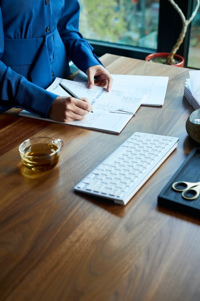 A clinician writing careful notes at a desk with tea and documents.