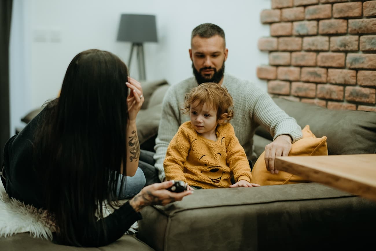 Two parents and their young child sitting together on a living room sofa.