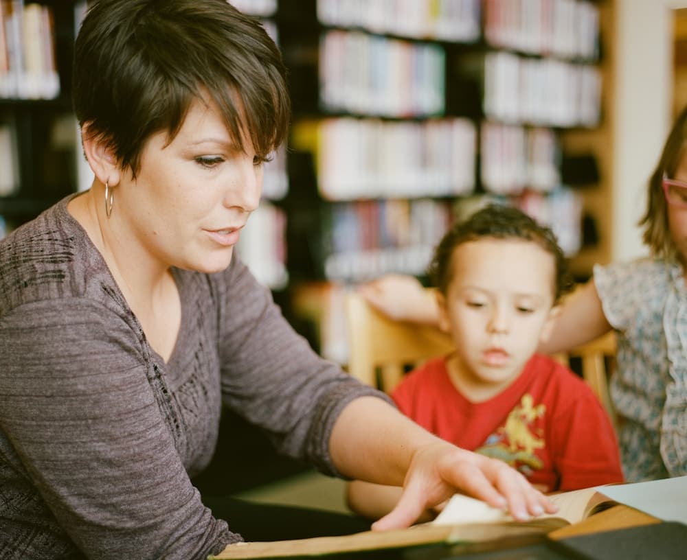 A teacher reading with a young student in a school library.
